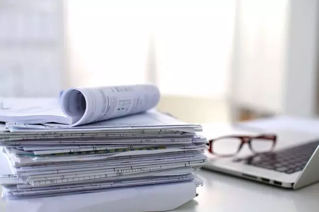 Стопка документов на столе рядом с ноутбуком